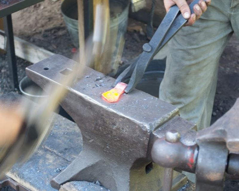 Hammer being swung onto hot iron resting on an anvil